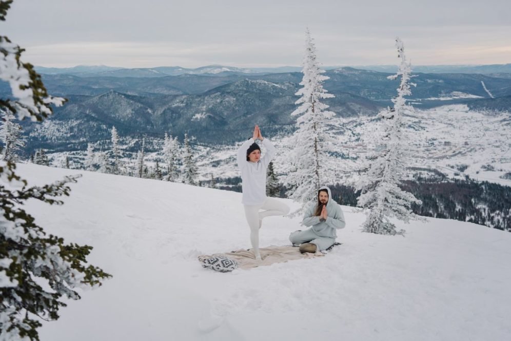 two people doing winter yoga on snowy mountain