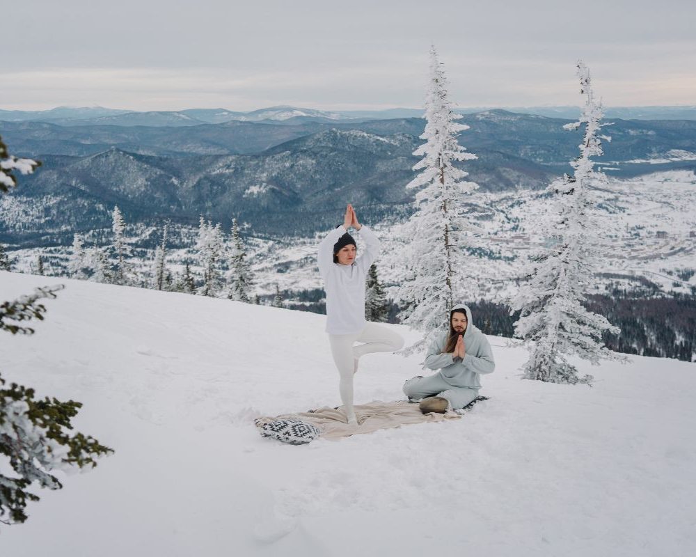 two people doing winter yoga on snowy mountain